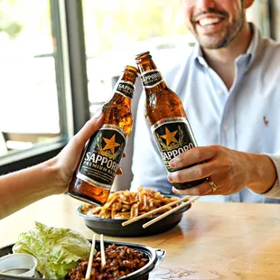 two people toasting beer bottles