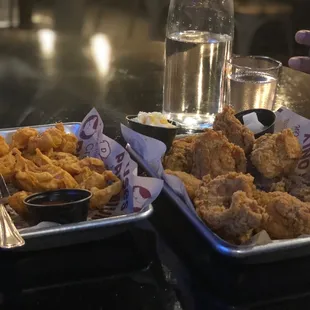 two trays of fried chicken and a glass of water