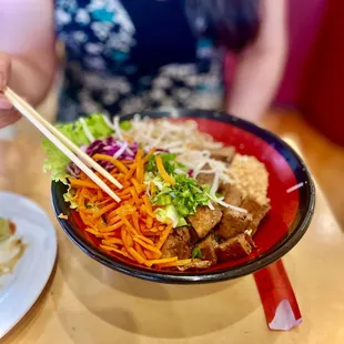 a woman holding chopsticks over a bowl of food