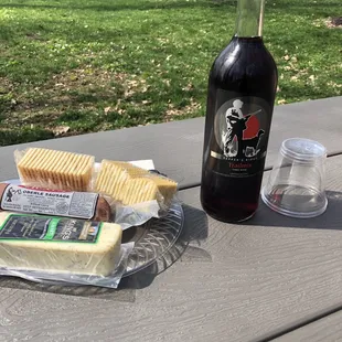 a bottle of wine, cheese and crackers on a picnic table