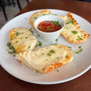 a white plate with four pieces of pizza and a small bowl of sauce