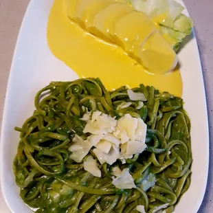a plate of green pasta with a side salad