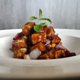 a plate of tofu with sauce and a sprig of mint