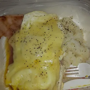 2 slabs of ham buried under 2 over medium eggs covered in cheese with a side of grits
