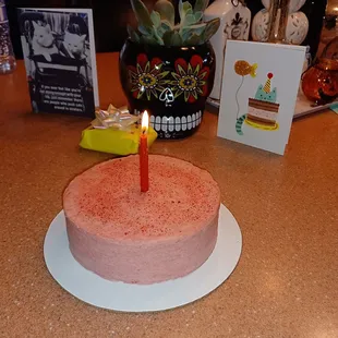 a pink cake with a single lit candle