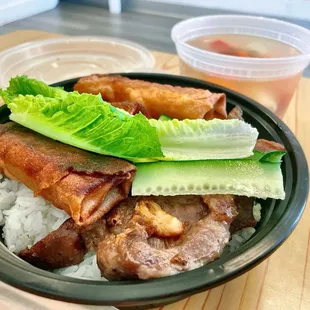 BBQ pork rice plate with fried egg rolls and a soup on the side.