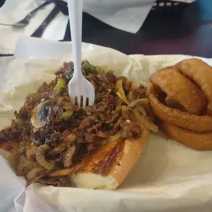 Half size Philly cheese steak with provolone cheese onions rings side.