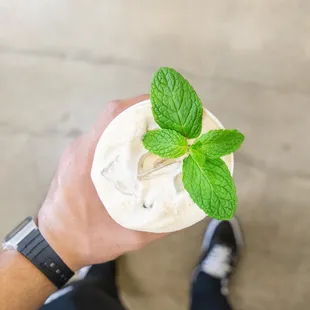 a person holding a cup of ice cream with a sprig of mint