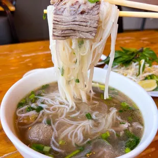 a bowl of beef and noodles with chopsticks