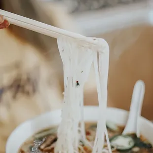 a person holding chopsticks above a bowl of noodles