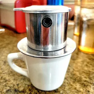 Cà phê sữa nóng is Vietnamese hot coffee with sweet condensed milk. This shows their pour-over device on top of a mug.