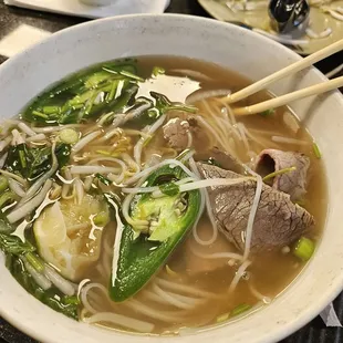 a bowl of beef and vegetable soup with chopsticks