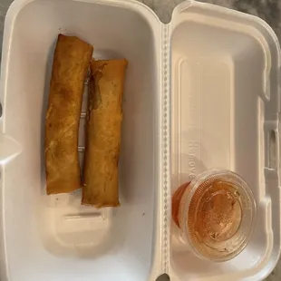 a plastic container with two fried spring rolls and a drink