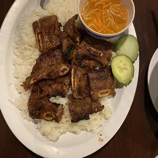 Bone in grilled beef short ribs with white rice, garnished with cucumbers.