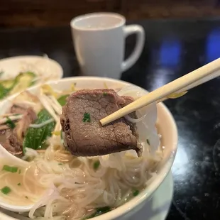 a bowl of beef and noodles with chopsticks