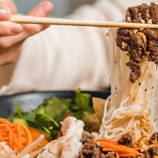 a person holding chopsticks over a bowl of noodles
