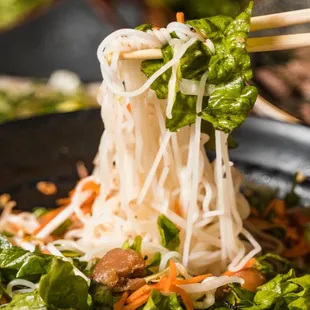 chopsticks lifting noodles out of a wok