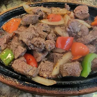 beef, peppers, and onions cooking in a skillet