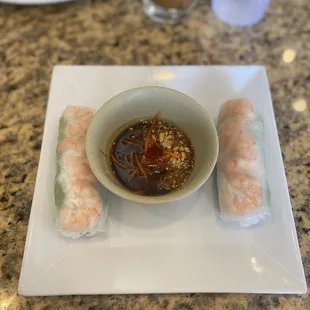 a bowl of dipping sauce and two spring rolls