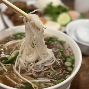 a person holding chopsticks over a bowl of soup