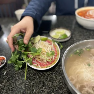 a person preparing a bowl of pho noodle