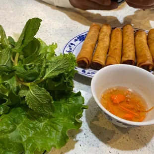 a plate of spring rolls, lettuce, and a bowl of dipping sauce