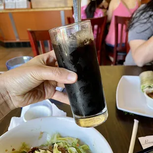 a person holding a glass of soda over a bowl of salad