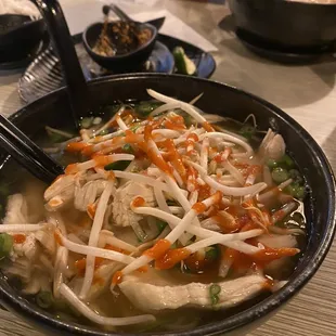 a bowl of chicken noodle with chopsticks