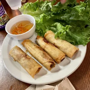 a plate of spring rolls, lettuce, and dipping sauce