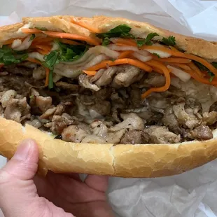 a hand holding a sandwich with meat and vegetables