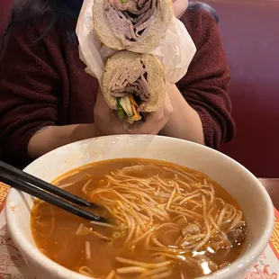 a woman holding a sandwich over a bowl of soup