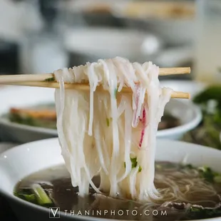 a person holding chopsticks over a bowl of noodles