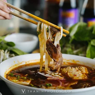 a person holding chopsticks over a bowl of soup