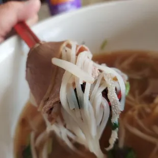a person holding chopsticks over a bowl of soup
