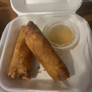 two fried spring rolls in a styrofoam container