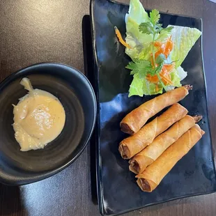 a plate of spring rolls and a bowl of dipping sauce