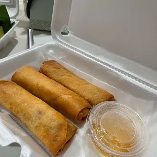 three fried spring rolls in a styrofoam container