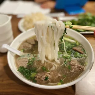a person holding chopsticks over a bowl of soup