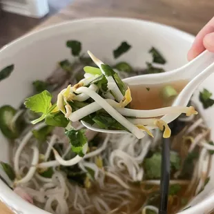 a person holding chopsticks over a bowl of soup