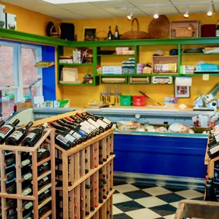 From the entrance, full wine racks, a cheese and deli case, and gift items on shelves.