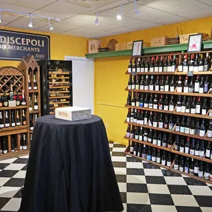 The back of the shop, one table, a wall of red wine, a Champagne chapel and a wine cooler.