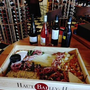 An extra-large charcuterie board in a wine crate with a selection of wine bottles in the background.