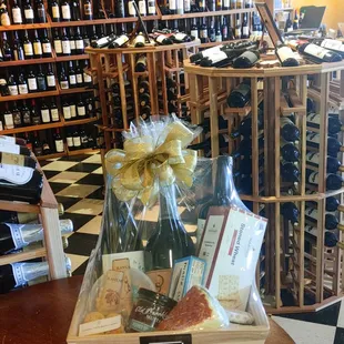 A shrink-wrapped gift box featuring bottles of wine, crackers, Melody's torta, mustard, sardines, among other gift items.
