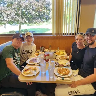 a group of people sitting at a table with plates of food