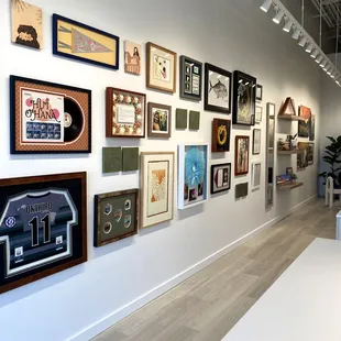 Gallery wall featuring framed sports jersey, record album, Hawaii art, baby keepsakes, gyotaku and more. Visit us to get inspired!