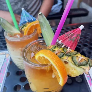 two cocktails with orange slices and umbrellas