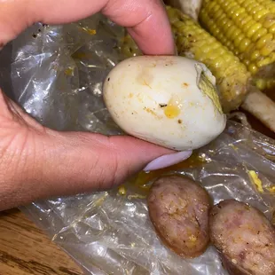 a hand holding a potato and corn on the cob