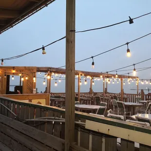 tables and chairs on a deck with string lights