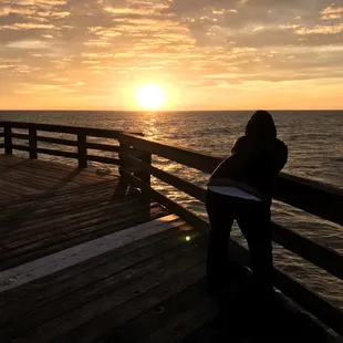 a person standing on a pier watching the sunset
