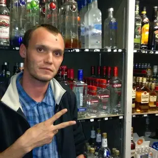 a man standing in front of a shelf of liquor bottles